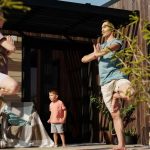 A family practicing yoga in tree pose on a sunlit porch, promoting health and mindfulness.