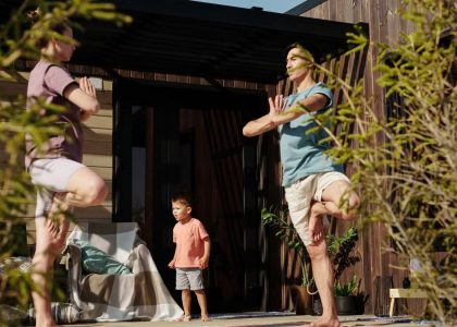 A family practicing yoga in tree pose on a sunlit porch, promoting health and mindfulness.